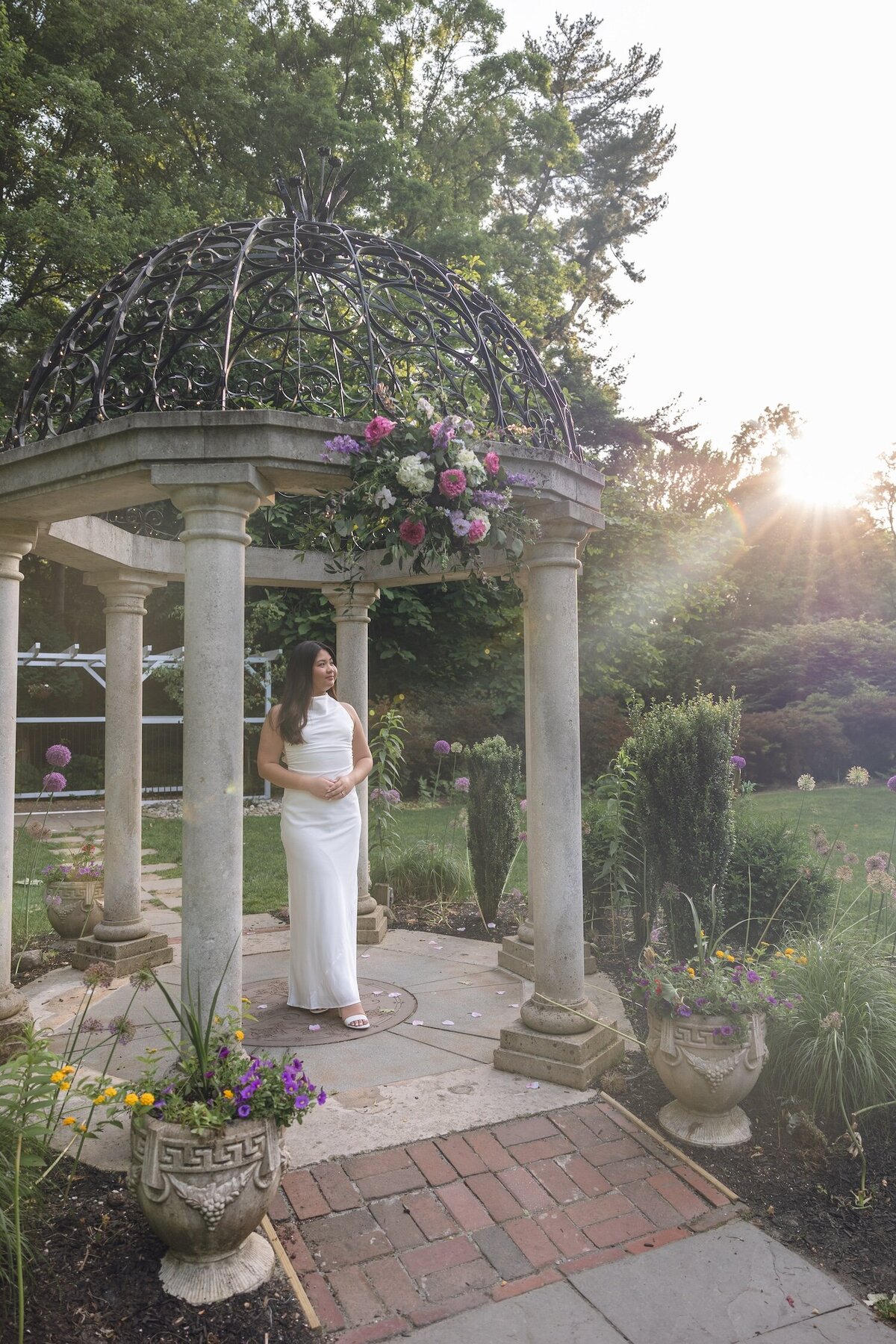 Bride-to-be walking under a flower-adorned stone pergola.