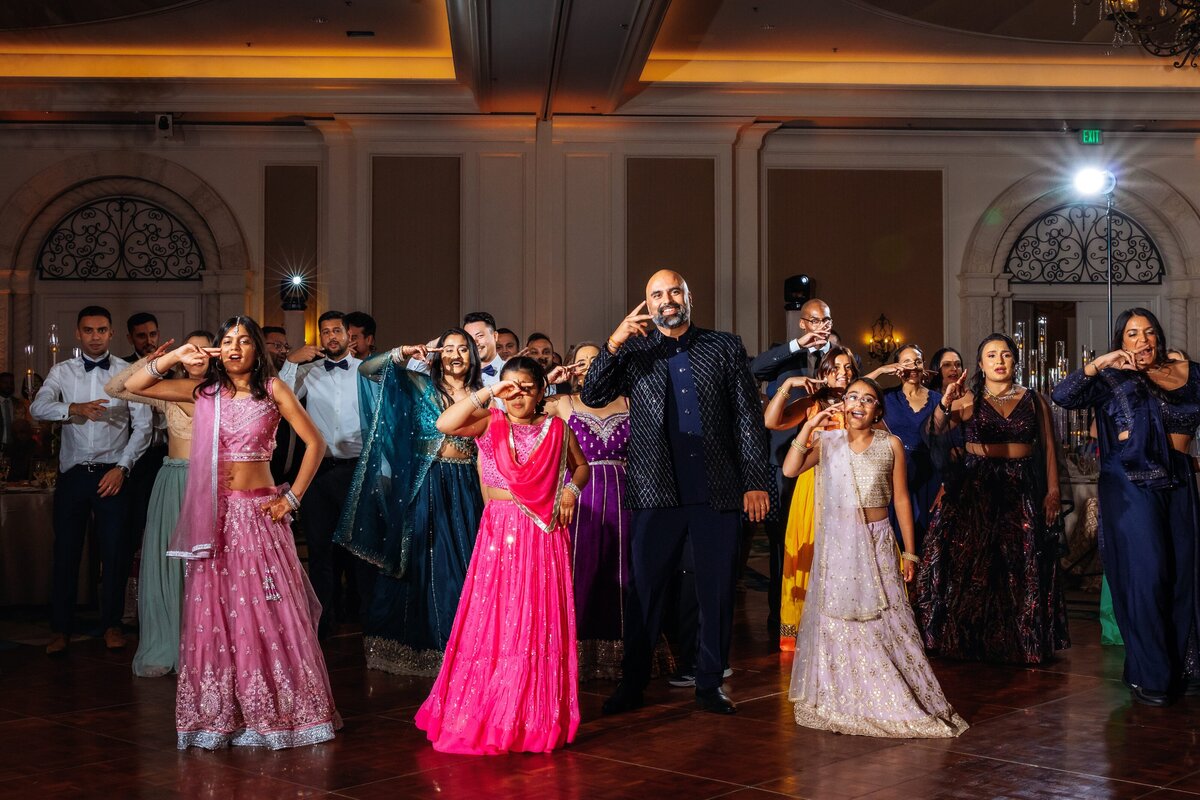 A group of guests dancing joyfully during the reception of an Indian wedding, dressed in vibrant traditional attire. Captured by Shannon, an Orlando, Florida Indian Wedding Photographer.