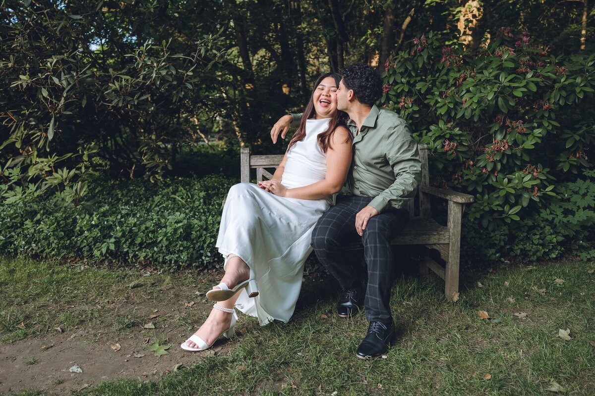 Bride-to-be sitting on a stone bench leaning into groom-to-be.