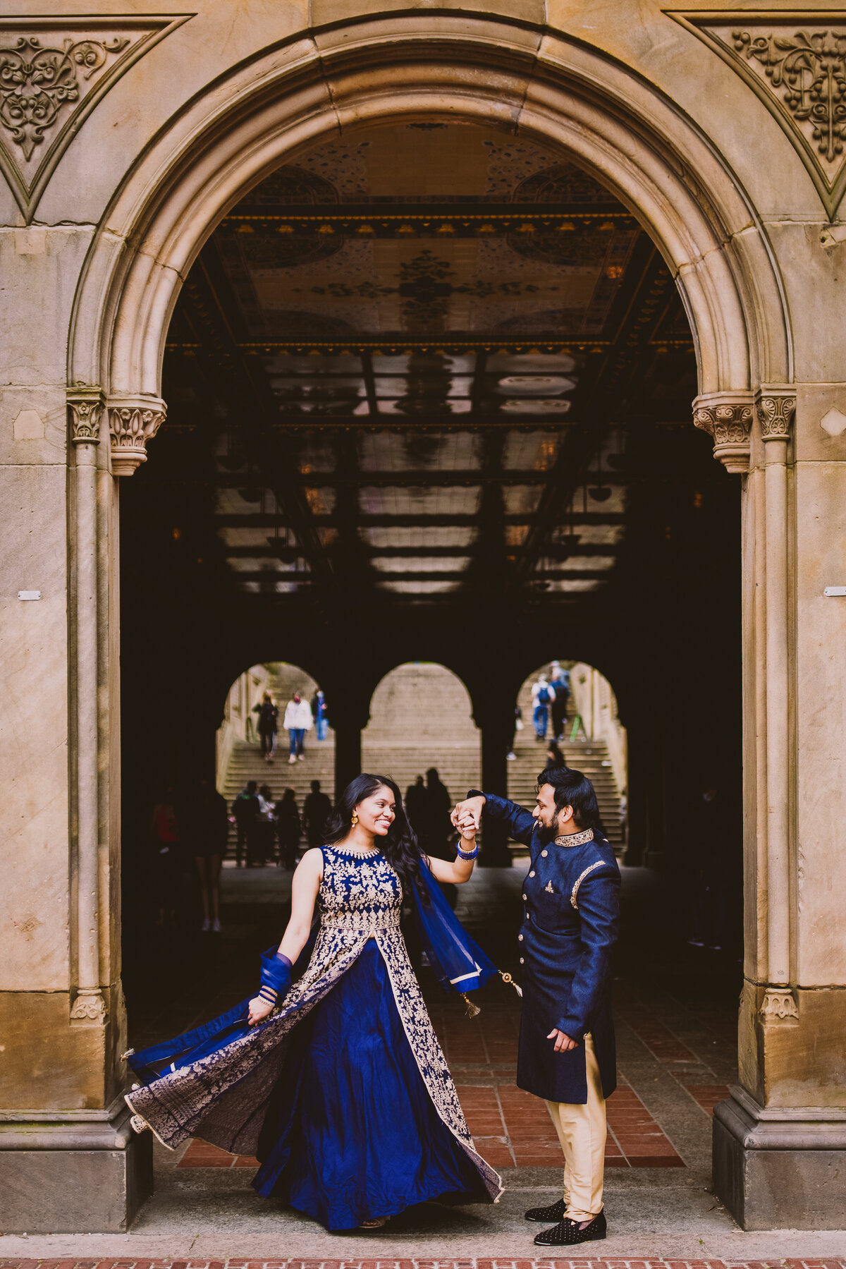 Groom twirling bride in blue indian outfits at the bethesda terrace under the arches at central park