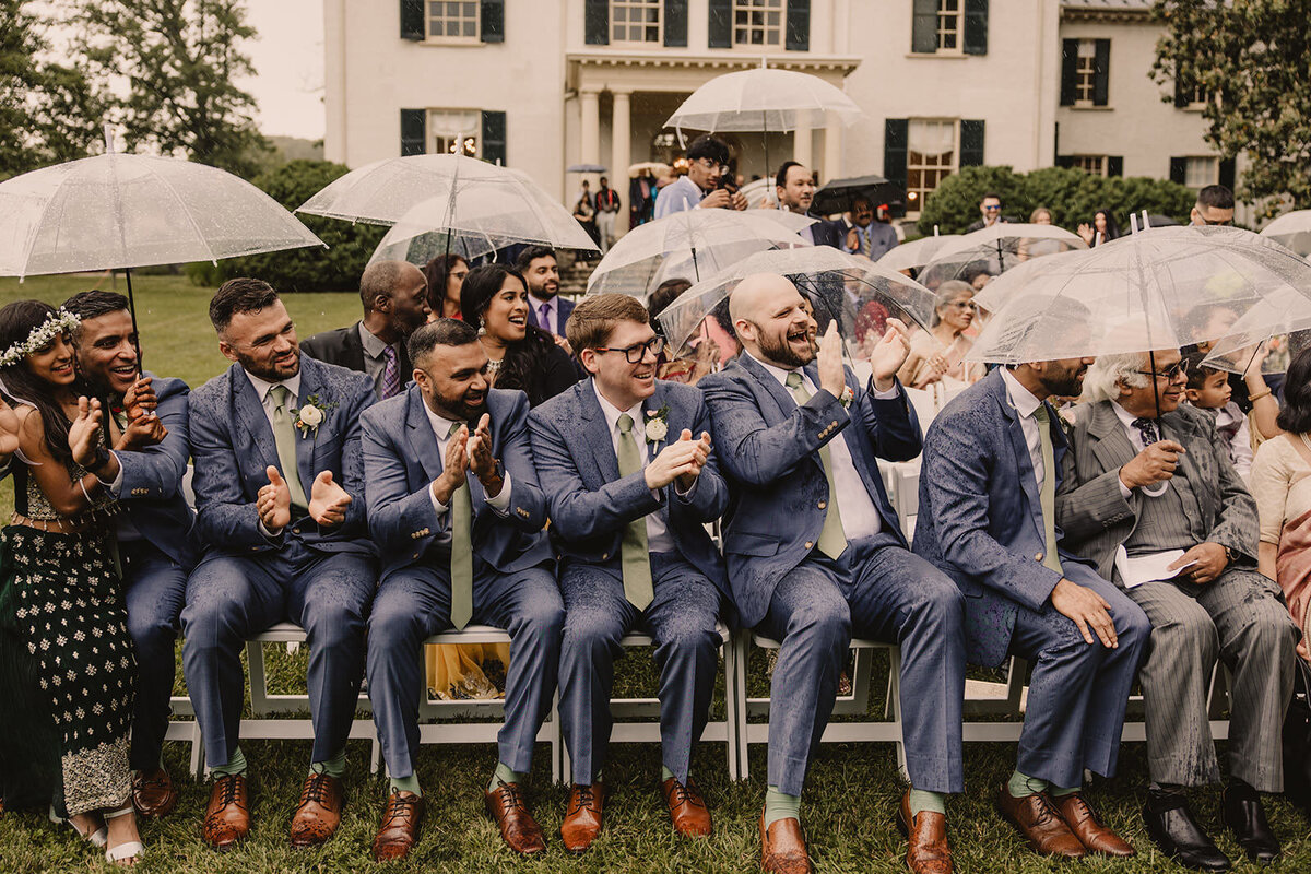 Wedding guests sitting at a ceremony holding clear umbrellas 