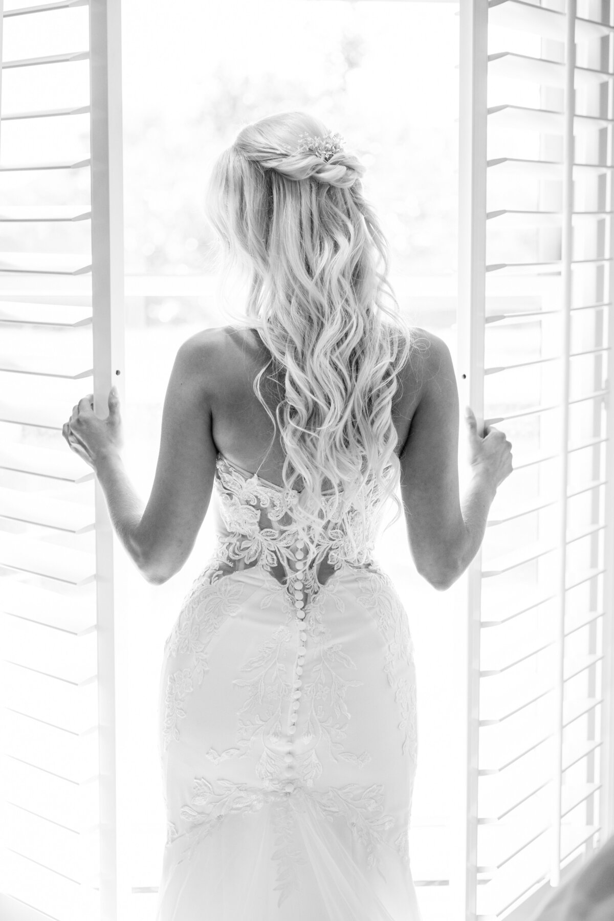 Black and white picture of blond hair bride opening the window