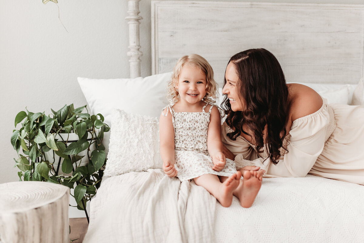 mom looking at little girl on daybed in milestone photographer's studio