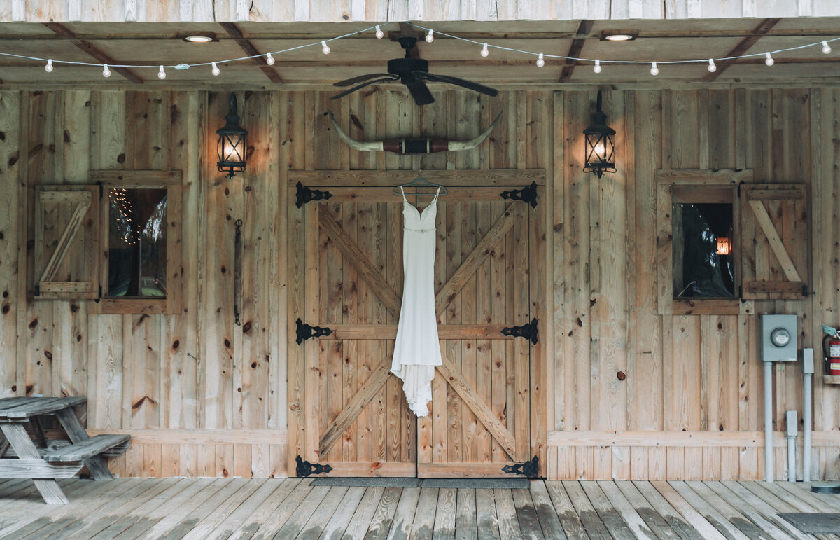 Wedding gown hangs on a rustic barn door under string lights at The Gentry Farm in Danville, Virginia.