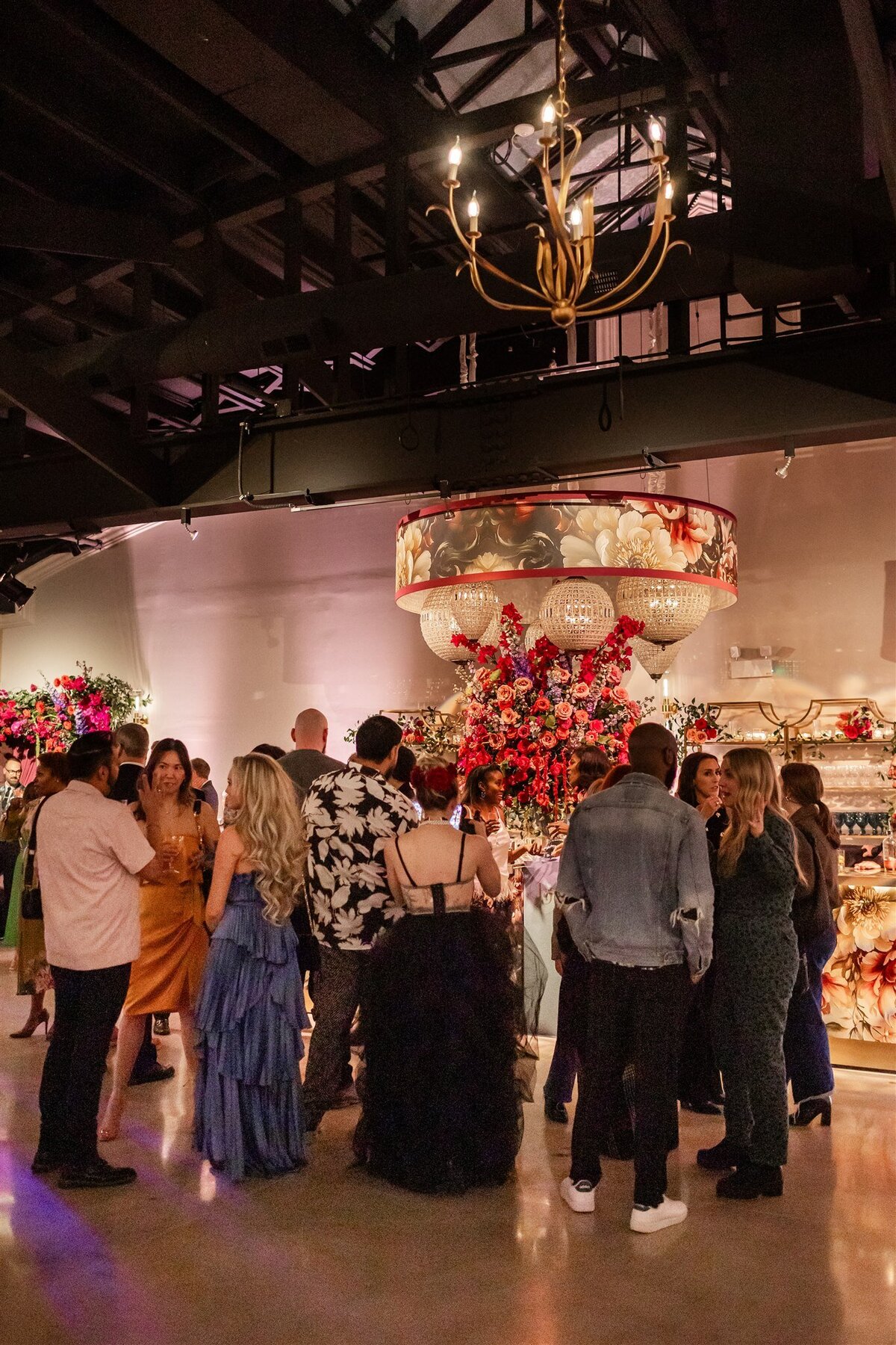 Large gathering at a Baroque-themed event, with guests dressed in formal attire mingling amid lavish decor including gilded furniture, crystal chandeliers, and rich drapery in a grand, ornately detailed space
