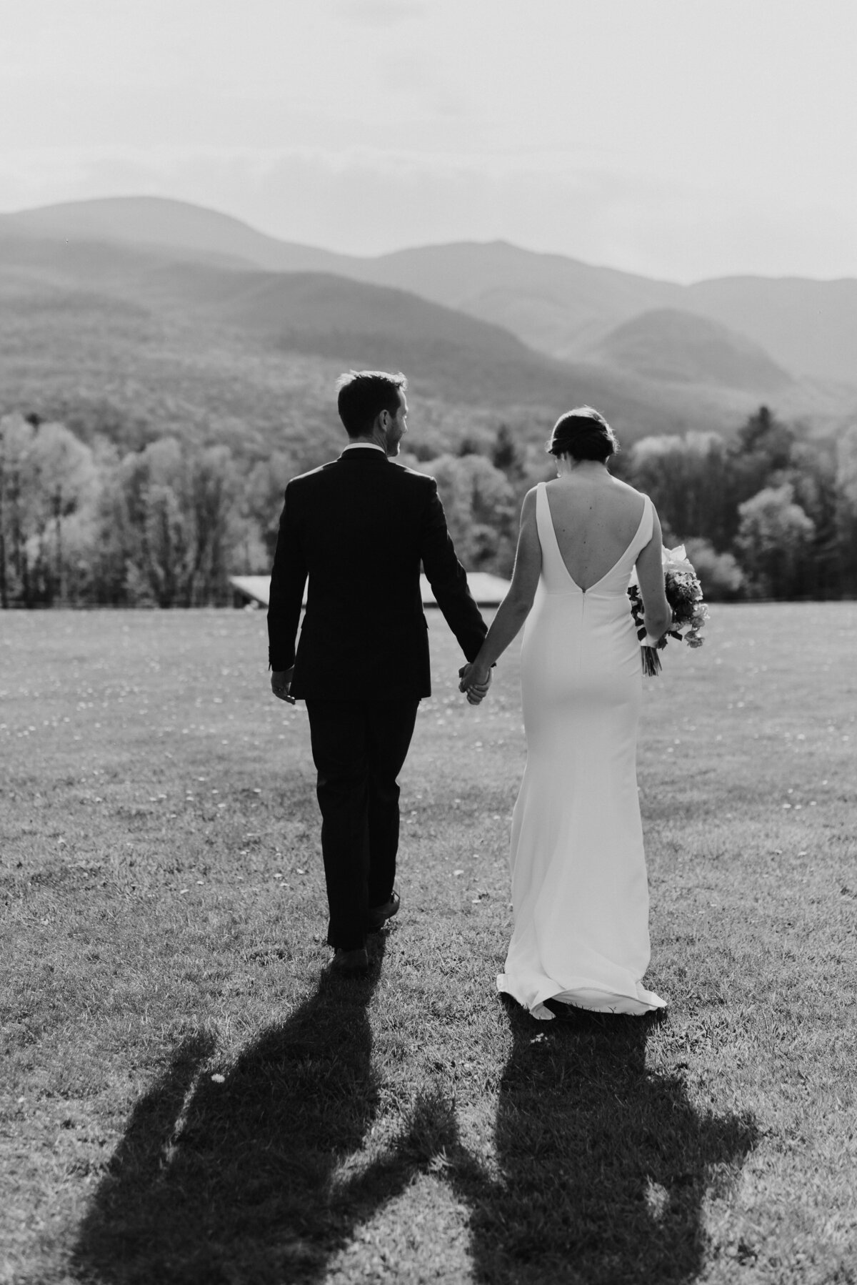 Wedding couple walking on mountaintop in Vermont in alyssa kristin gown with flowers by  Jayson Munn dEsign planned by lindsey leichthammer events
