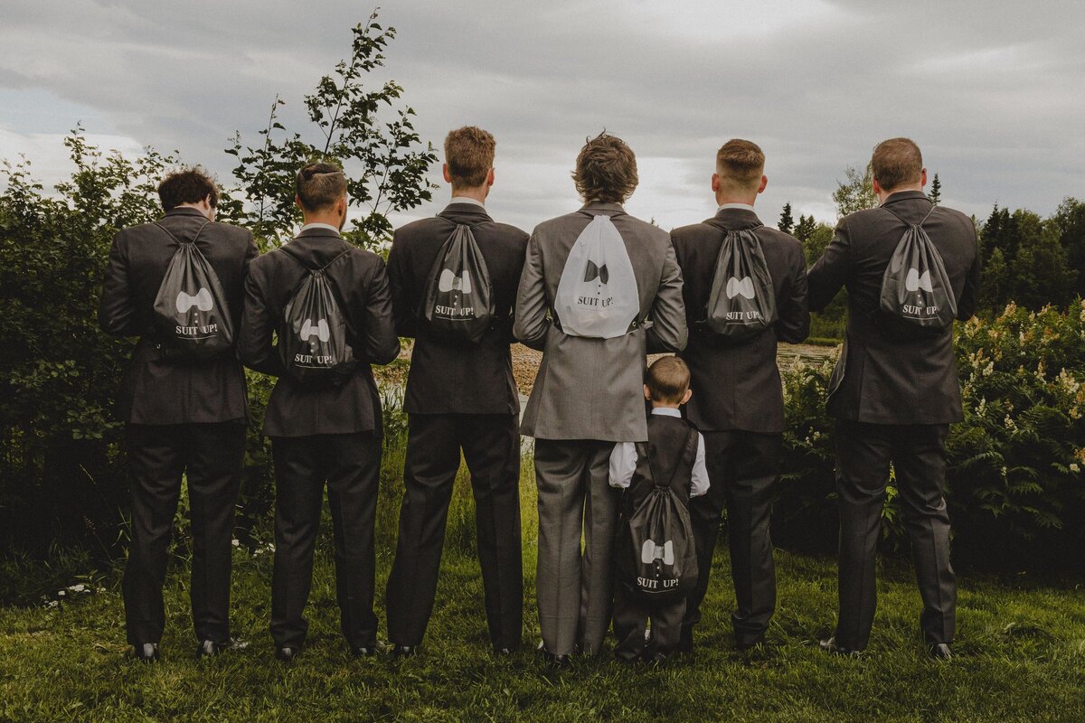 A group of groomsman pose with their backpacks, including the smallest member