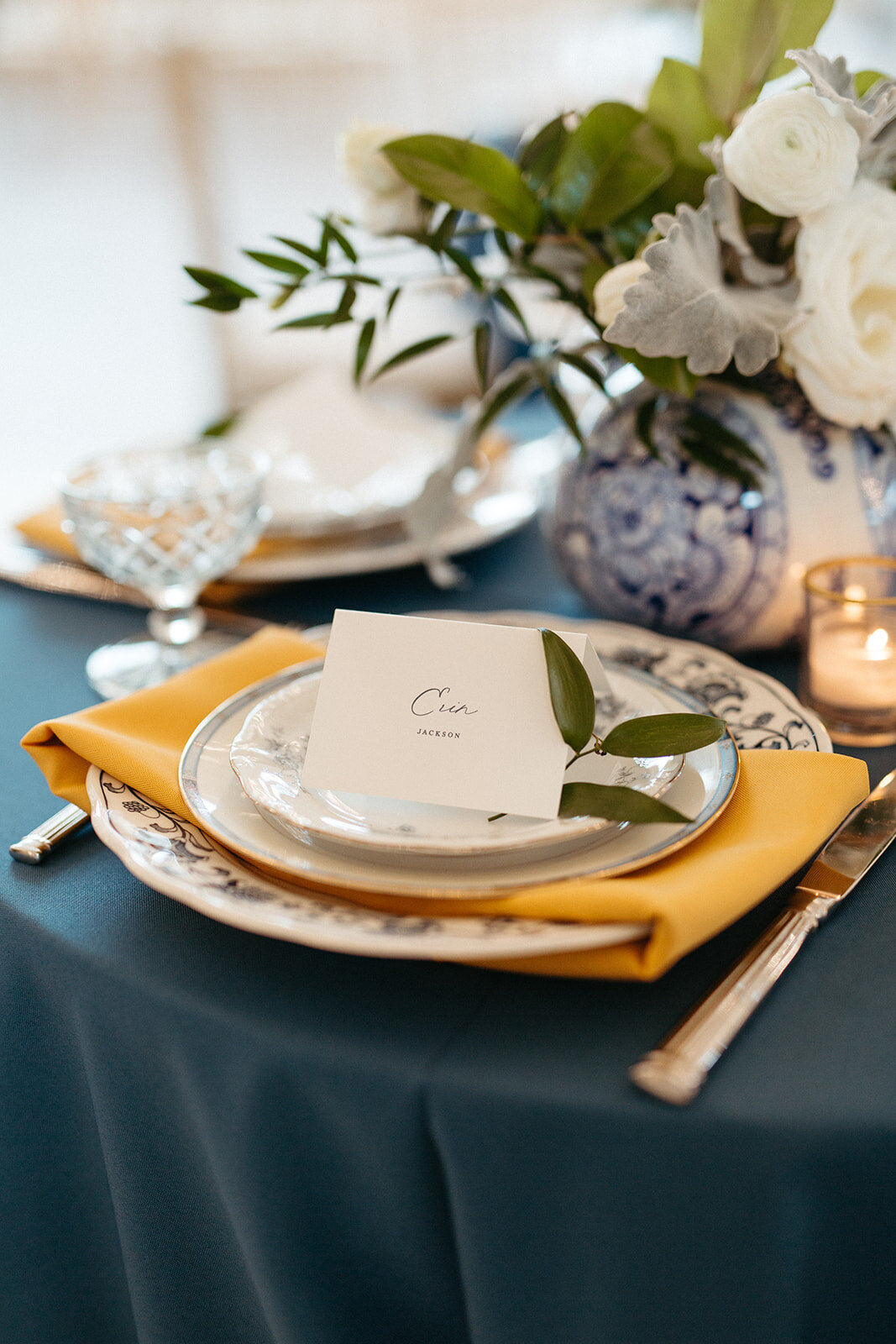 White place cards set on yellow napkin with white plates atop a table with blue line and florals.