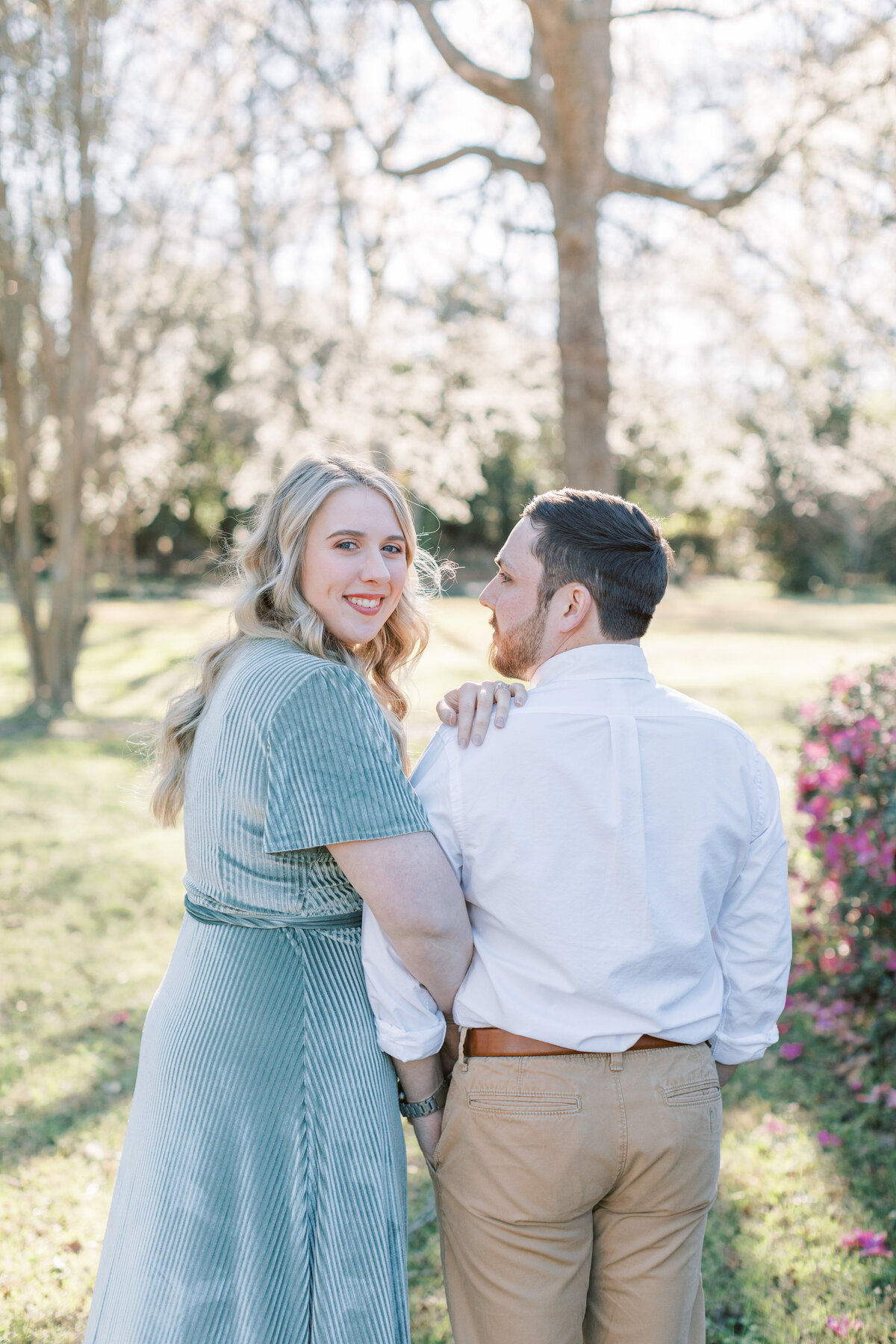 A couple stands in a park for their spring engagement photos.