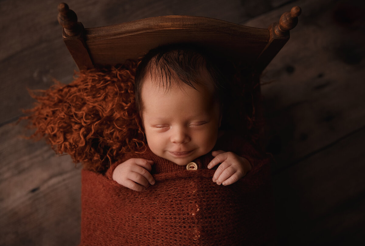 newborn boy laying in bed wearing rust orange snuggled in studio setting near bellevue