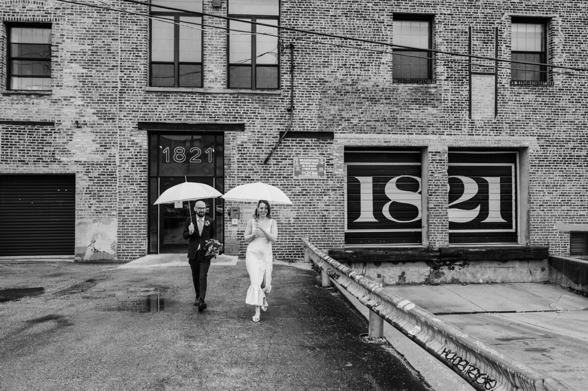 Bride and groom carry umbrellas while it rains on their chicago wedding