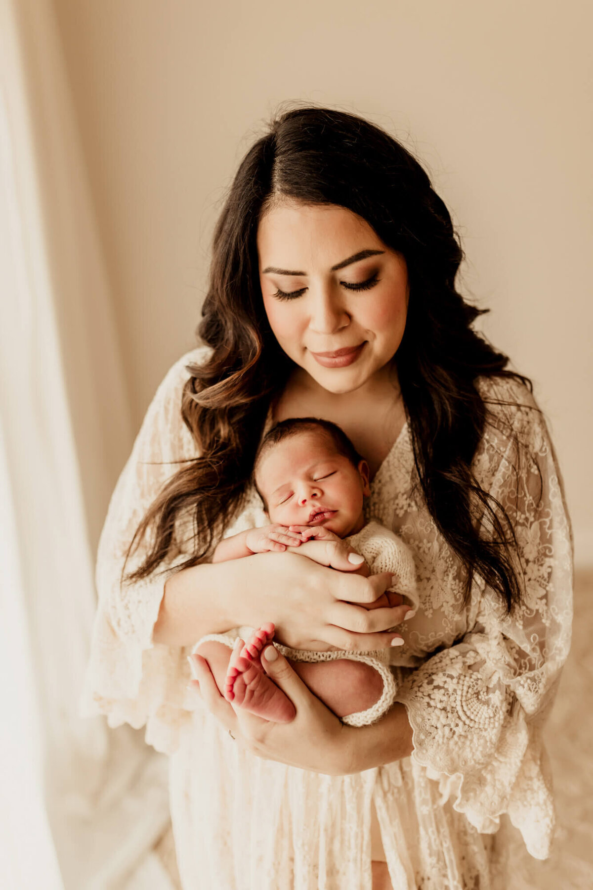 Mother with long dark brown hair holds her baby boy in her arms as she looks down at him.