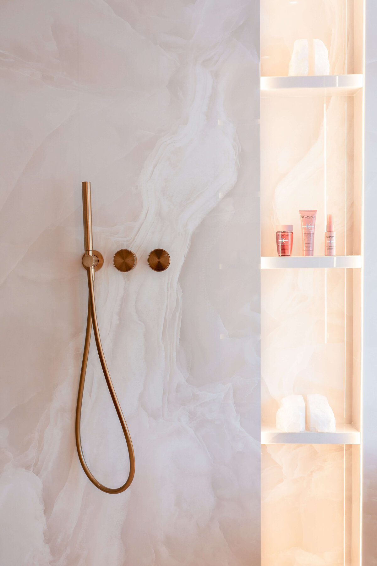 Rose gold shower hardware against a light pink marble wall.