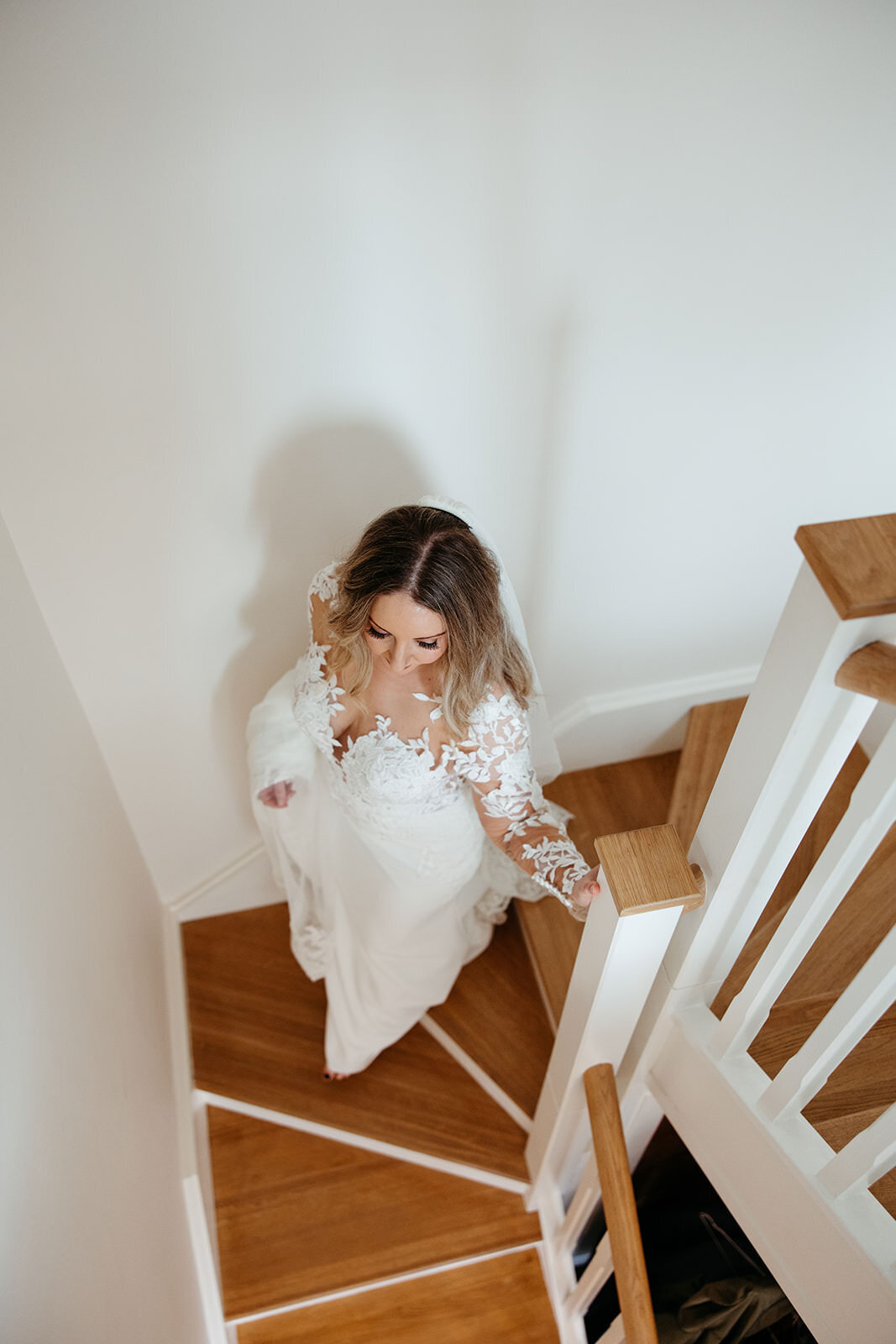 A bride ascending a wooden staircase, dressed in a white gown with lace sleeves
