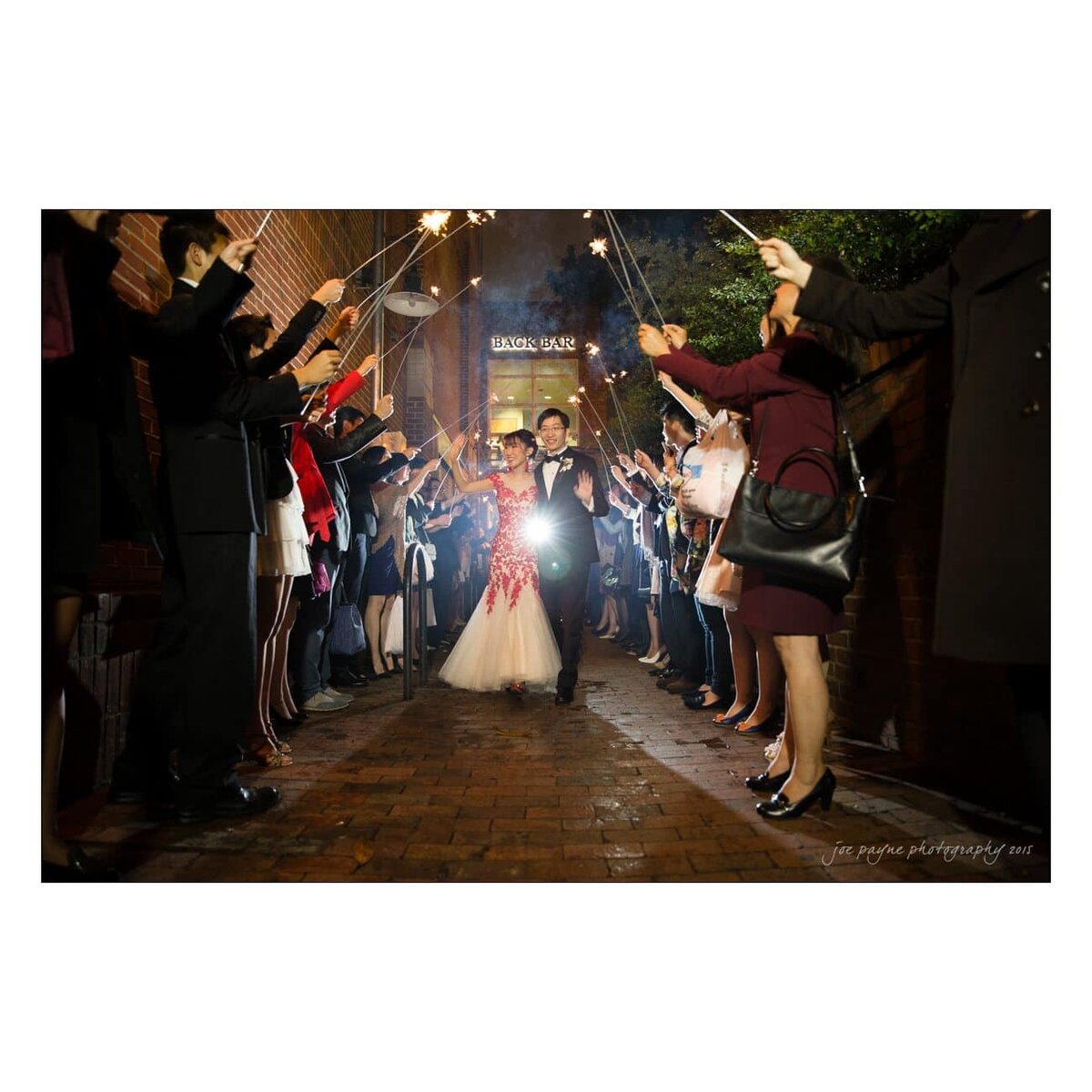 A bride and groom walking through a tunnel of sparklers held by guests.