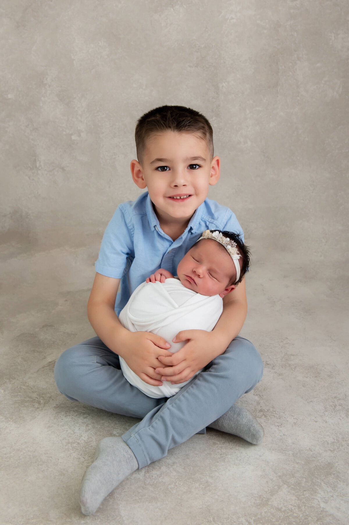 Big brother holding newborn baby girl on a beige background for their newborn photos