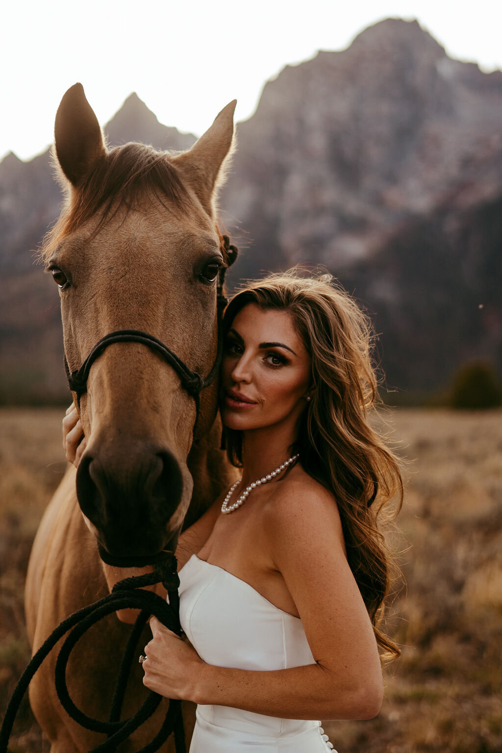 western chic bride poses with a horse as the sun sets below the Tetons of Jackson, Wyoming