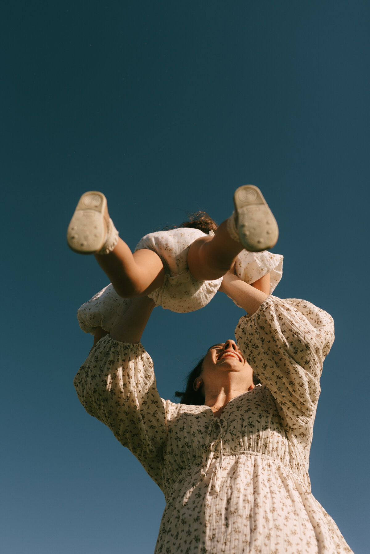 a mother swinging her daughter around and around with the deep blue sky above them.