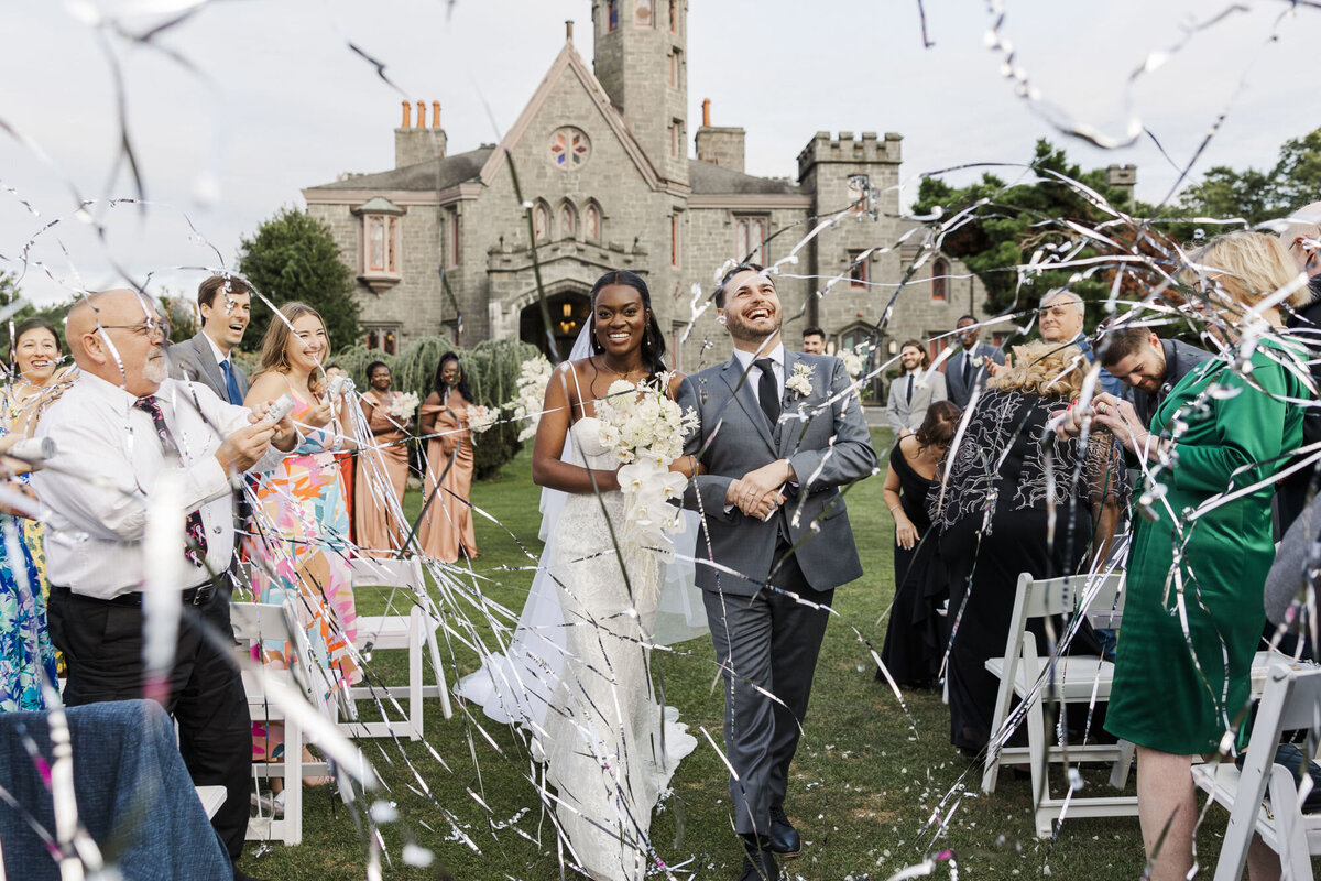 Newlyweds walk back up the aisle through streamers at a castle wedding captured by Hudson Valley wedding photographers