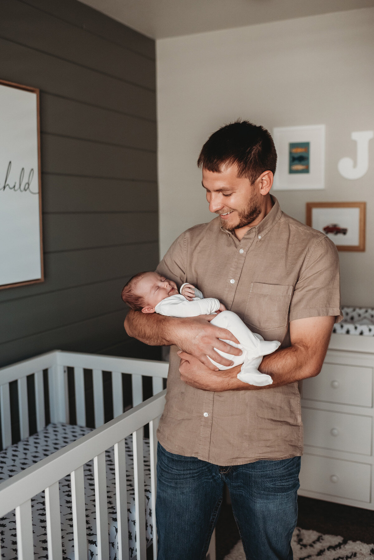 dad holding newborn baby in his nursery while they both smile