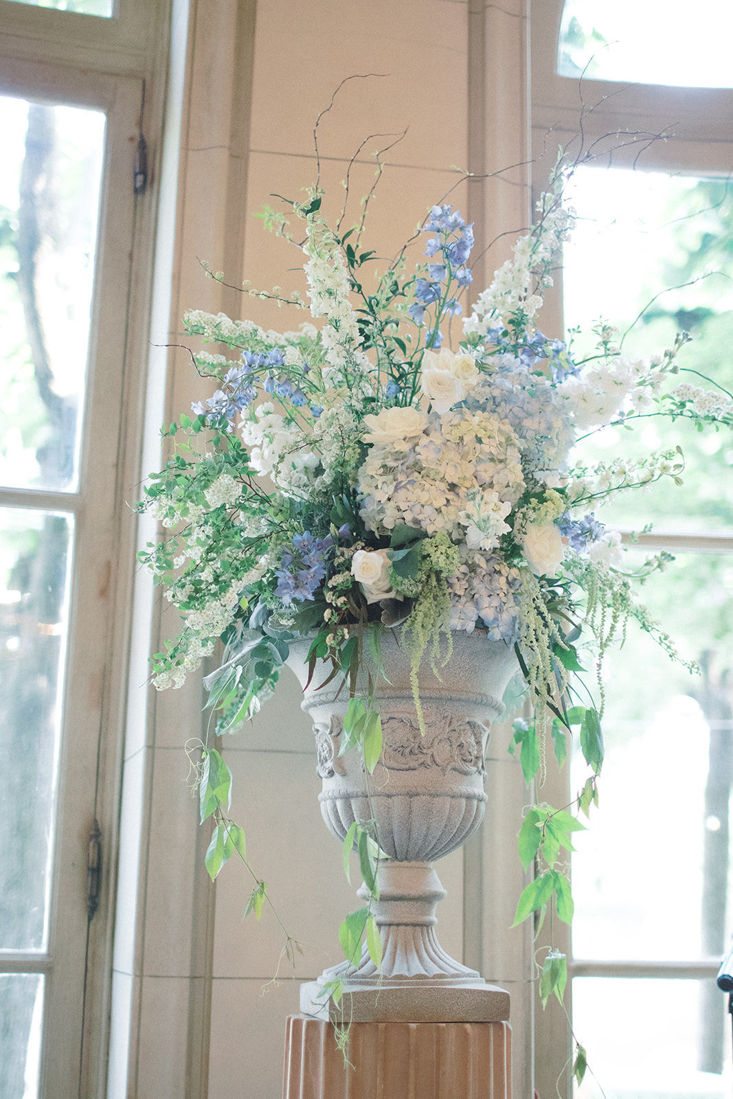 Large urn holding blue and white flowers and draping greenery as a backdrop for a wedding ceremony at the Meridian House in Washington, DC