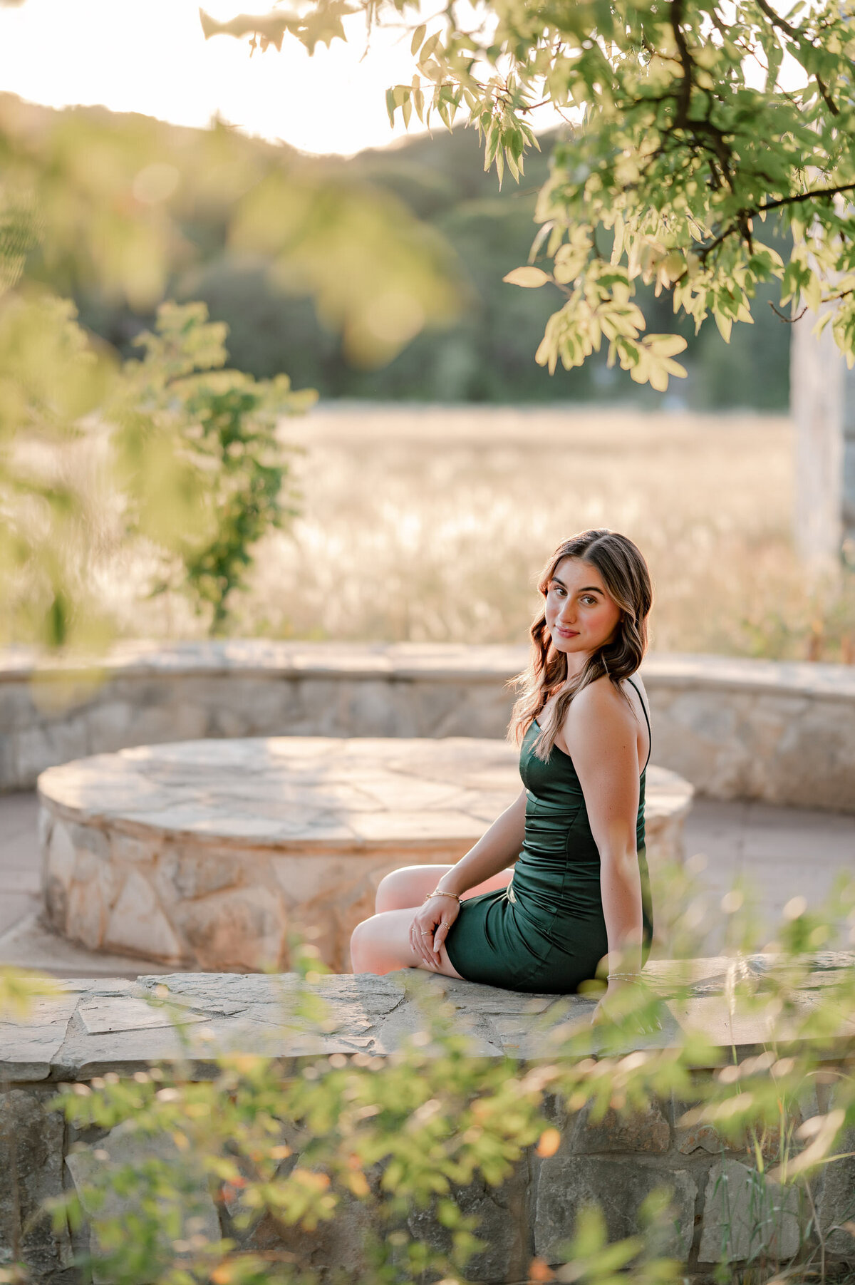 Glowing image through the trees of a senior girl in a green dress looking over her shoulder at the camera.