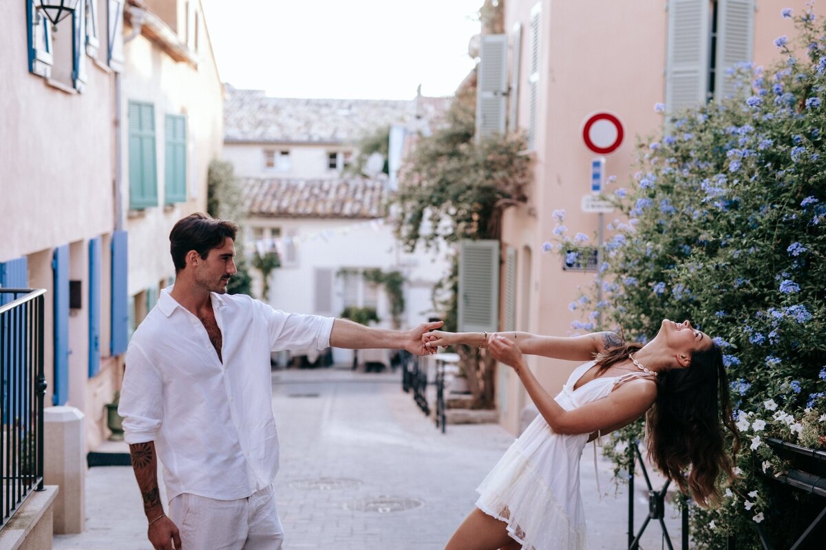 Man dancing with woman in the side streets of France with her arms out and head back having fun.