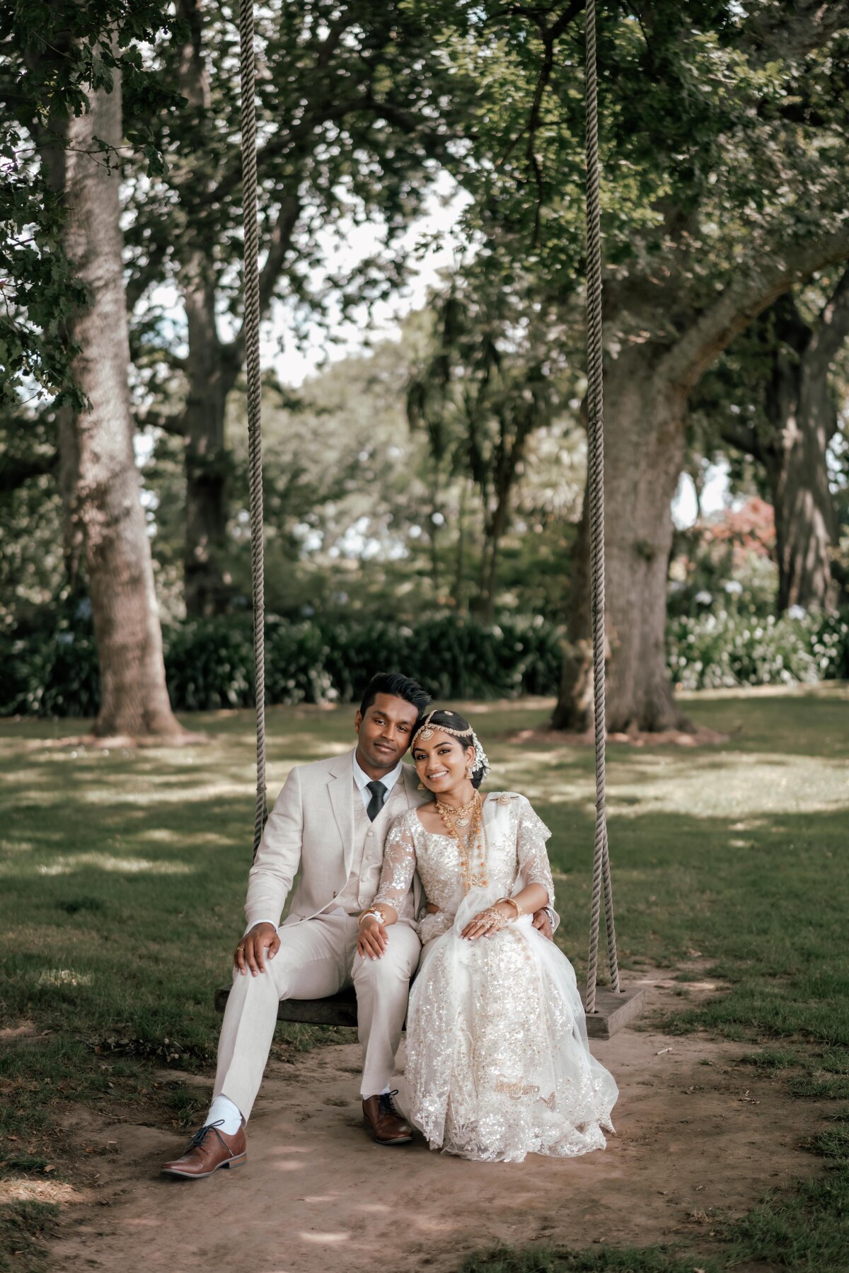 Bride and groom Tilly and Supun sitting on swing together outdoors surrounded by greenery during their hamilton wedding portraits, photographed by Zanthe Vorsatz.