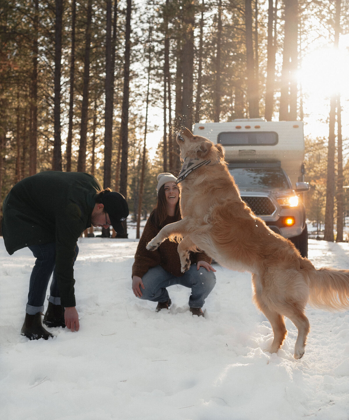 man and woman throw snowballs for their dog in the woods in Oregon