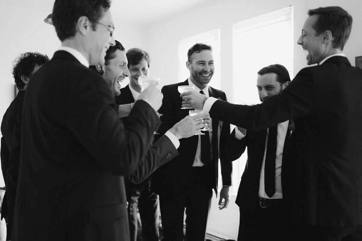 The groom and his groomsmen are drinking while laughing in Foxfire Mountain House, New York. Wedding Image by Jenny Fu Studio