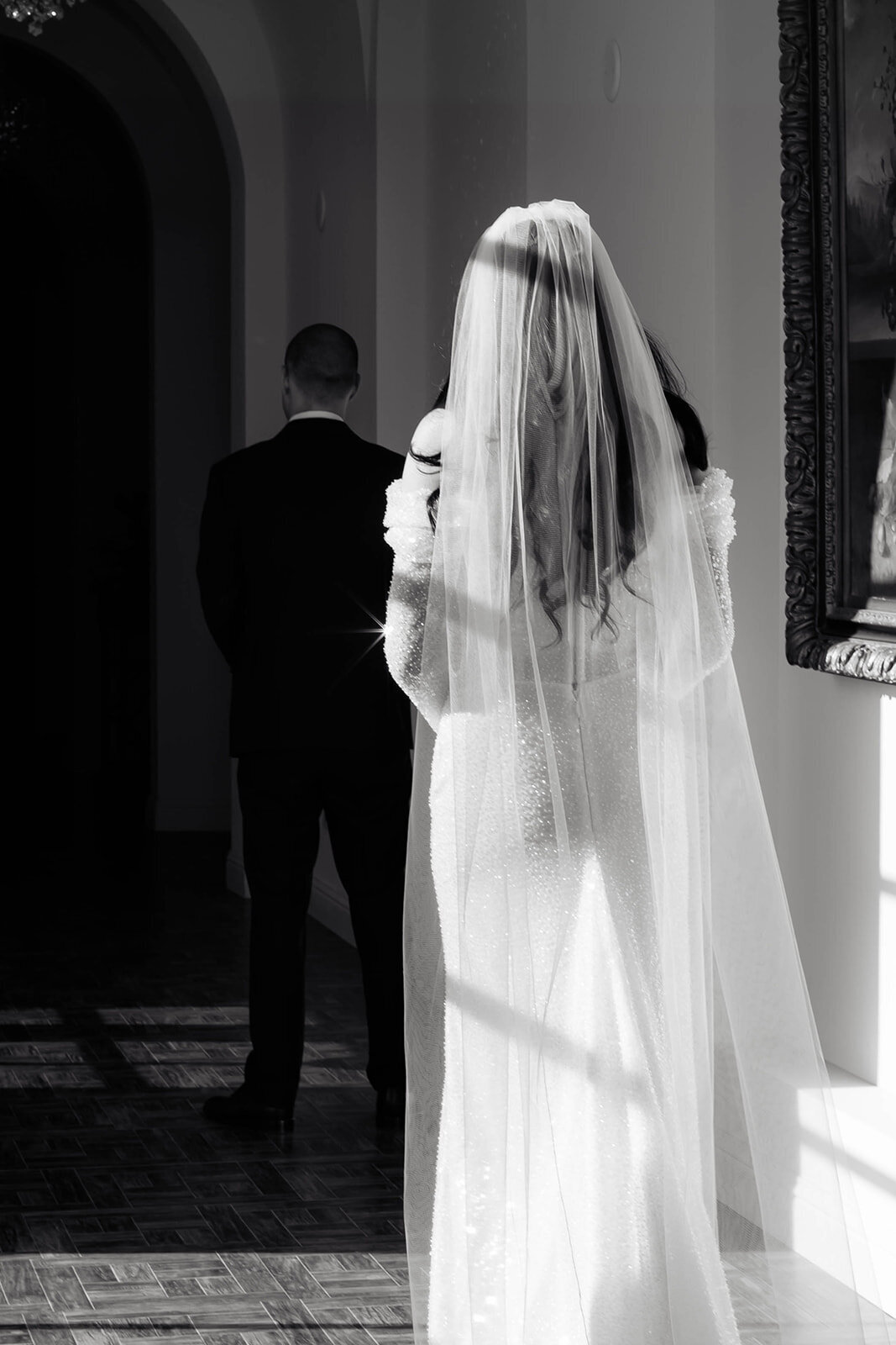 A bride in an elegant beaded gown approaches her groom for their first look, bathed in soft natural light. A cinematic and editorial wedding photograph capturing intimate anticipation.