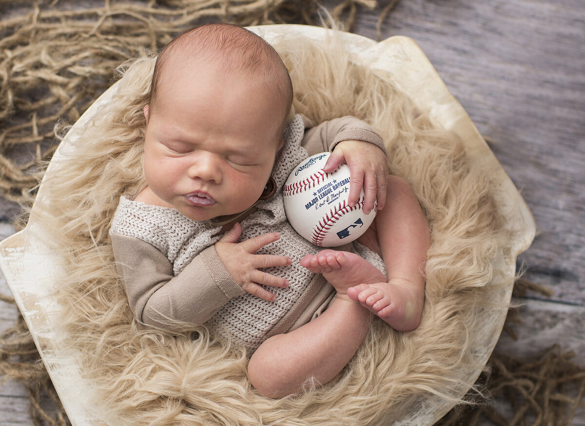 a newborn holding a baseball with light brown fur around him