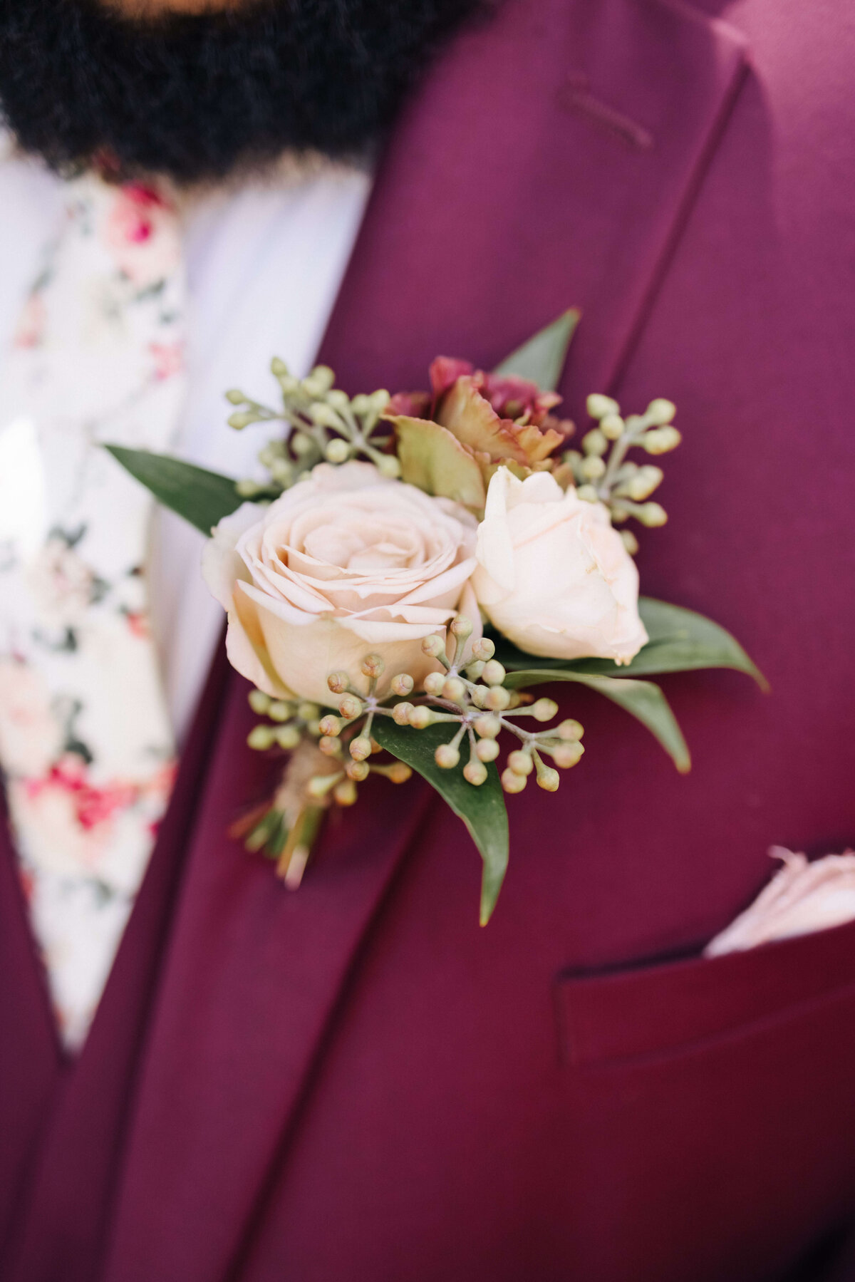 A groom in burgundy suit with a rose and lisianthus boutonniere