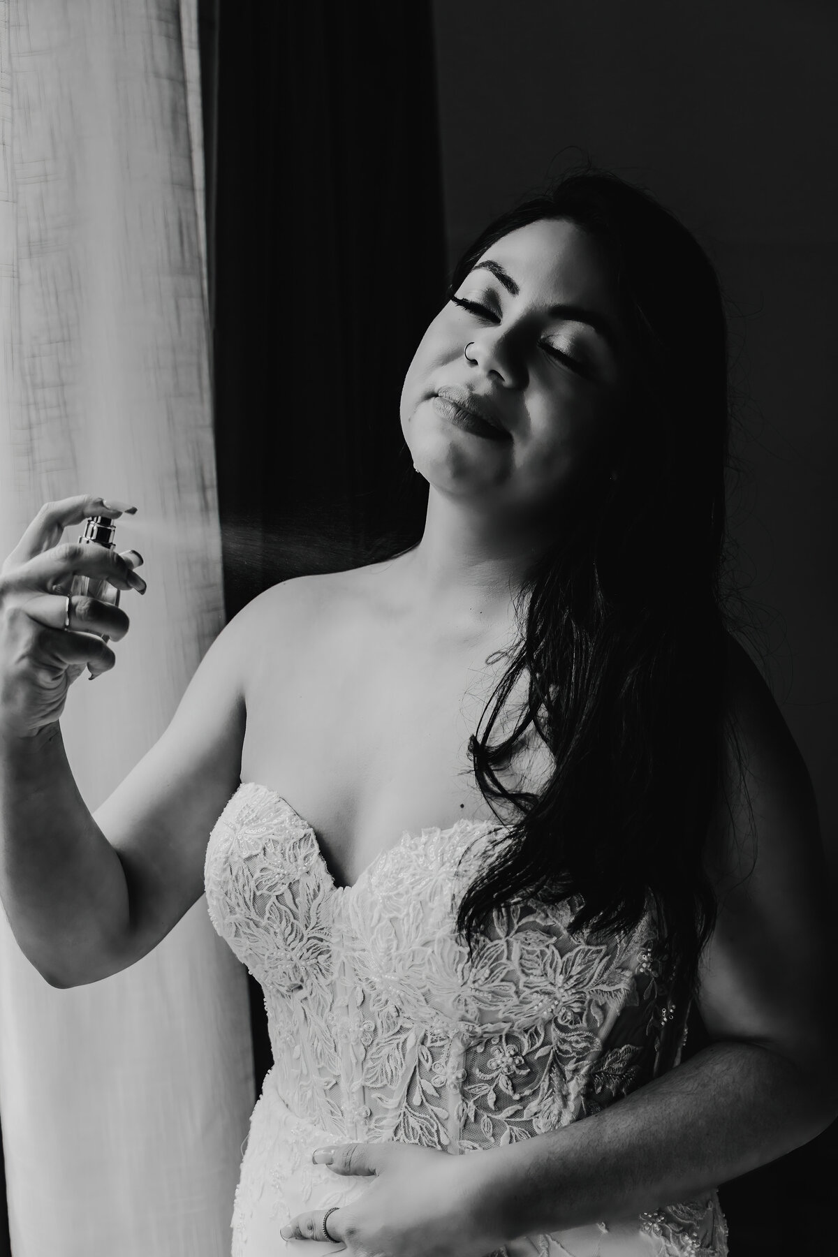 a black and white photo of a bride putting on perfume in her getting ready space