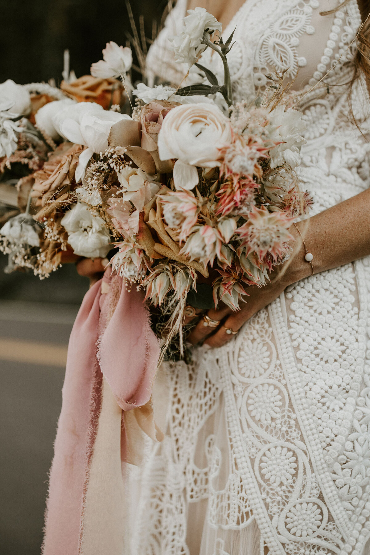 bride wearing ivory wedding gown holds bouquet of ivory and blush flowers with blush ribbon