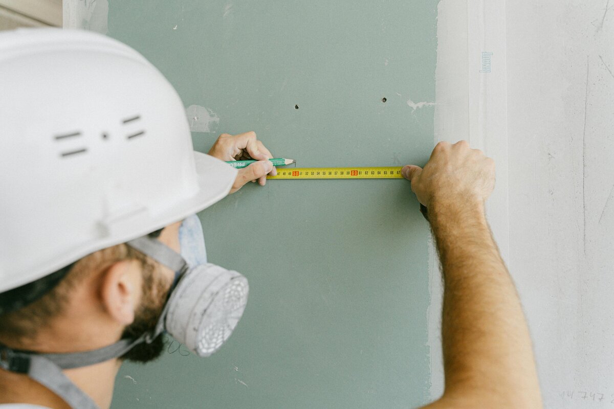 A contractor measuring wooden wall studs with a tape measure during a framing stage of a home renovation project.