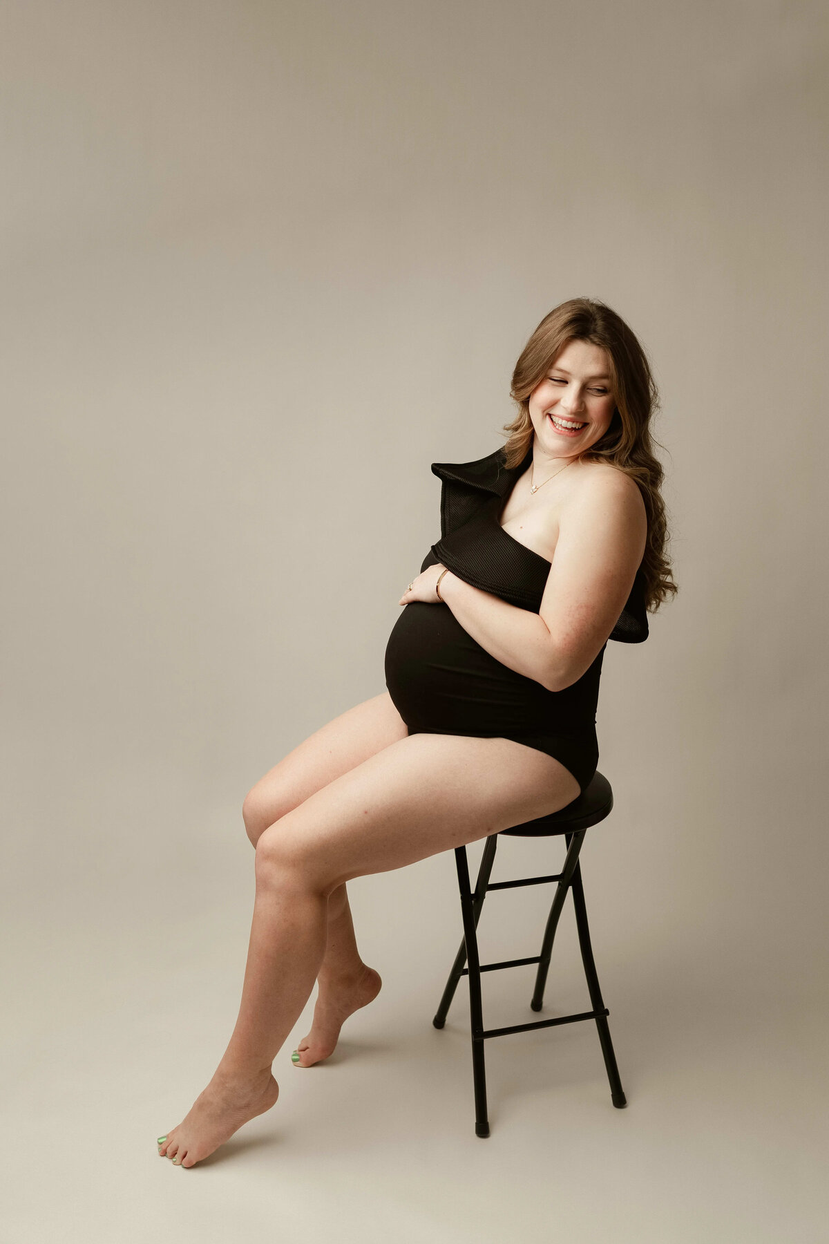 Fun maternity portrait in black bodysuit sitting on a stool in Minnesota