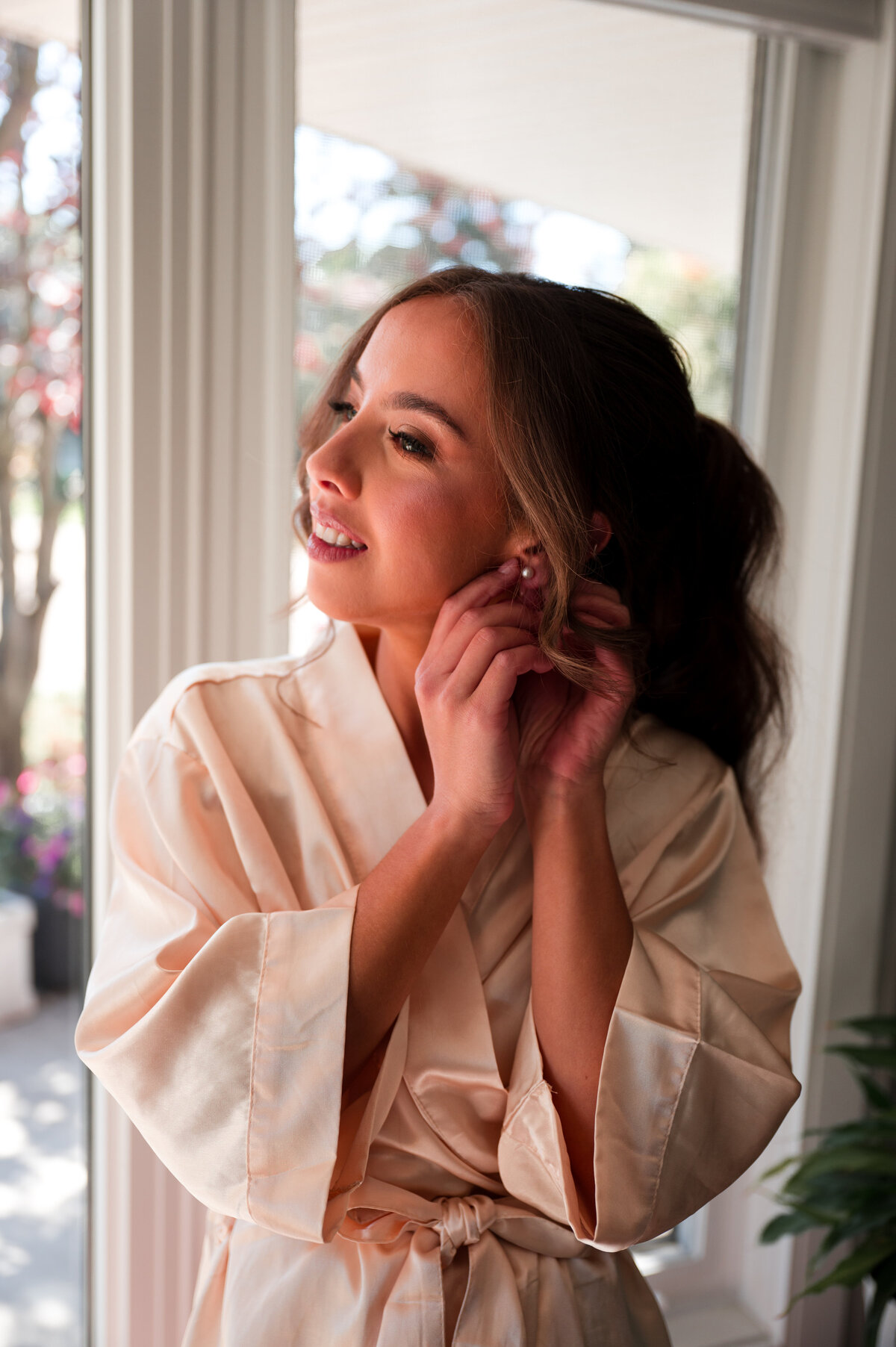 bride in a white robe putting earrings on