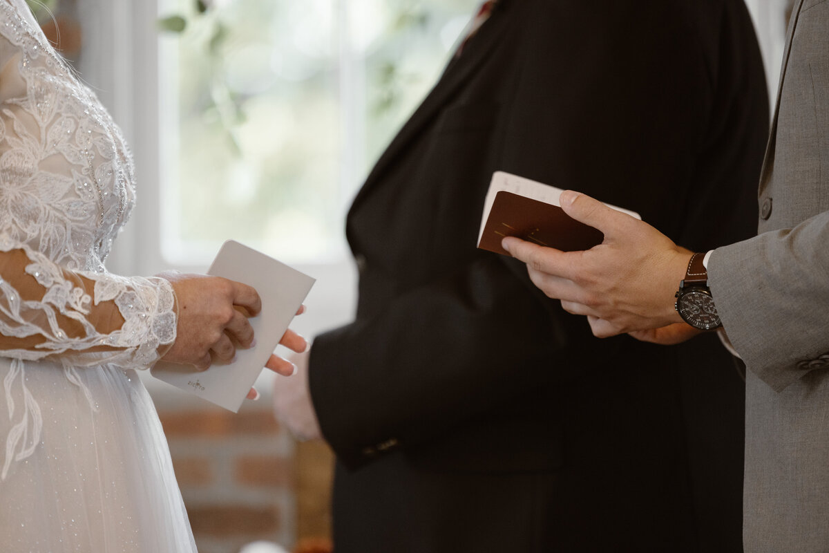 Close-up of a bride and groom holding personalized vow books during their indoor wedding ceremony, with an officiant standing between them.