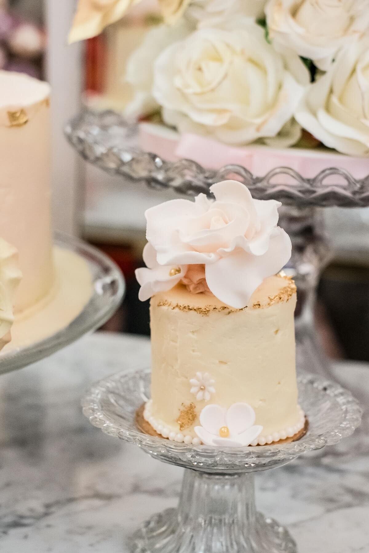 Miniature dessert cake with white sugar flowers on a small glass cake stand