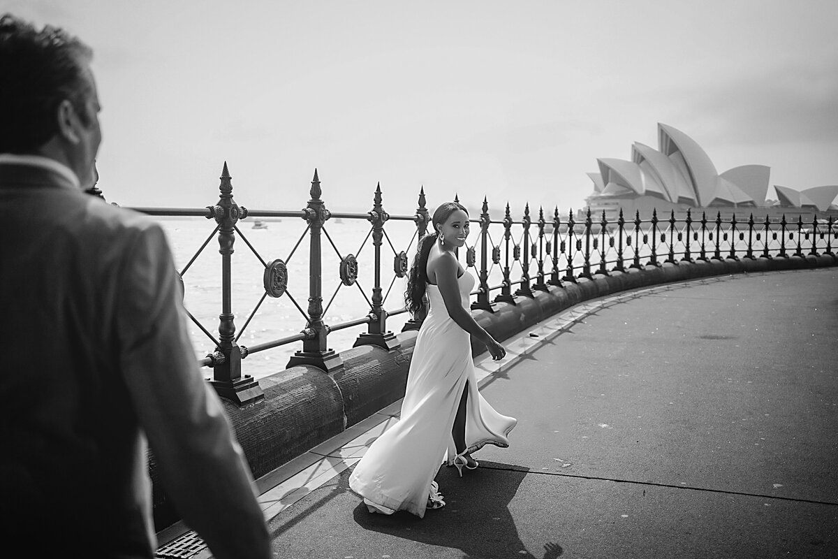 Woman in white gown walks ahead of her husband looking back smiling as he follows