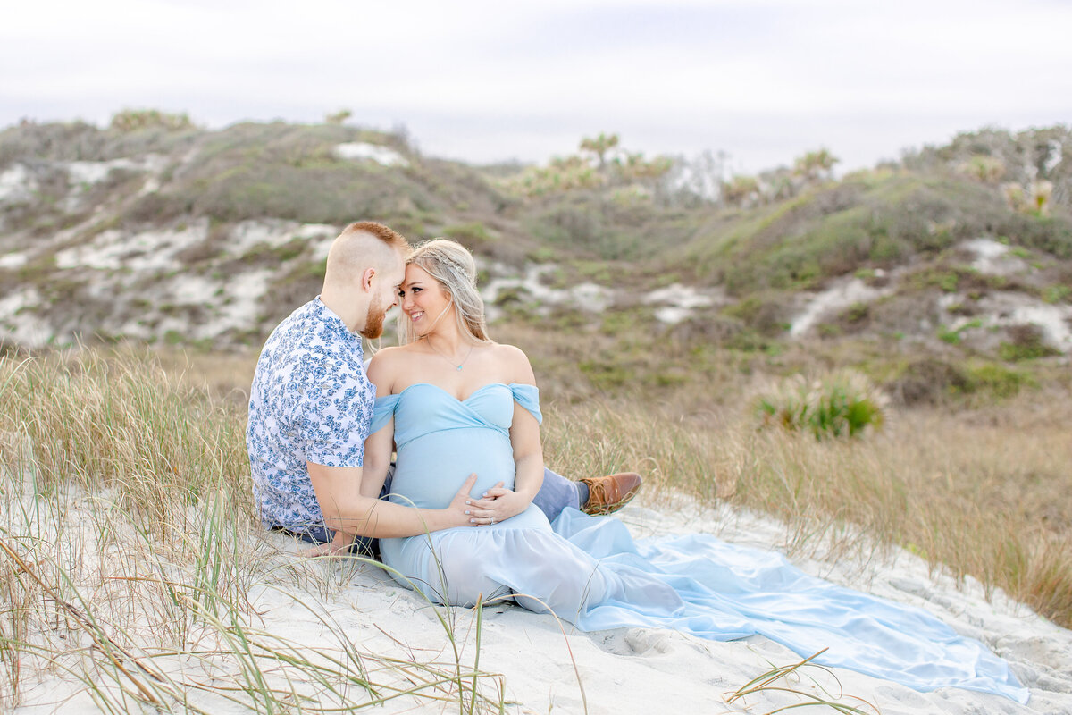 soon to be mom and dad sitting on the beach during their maternity session