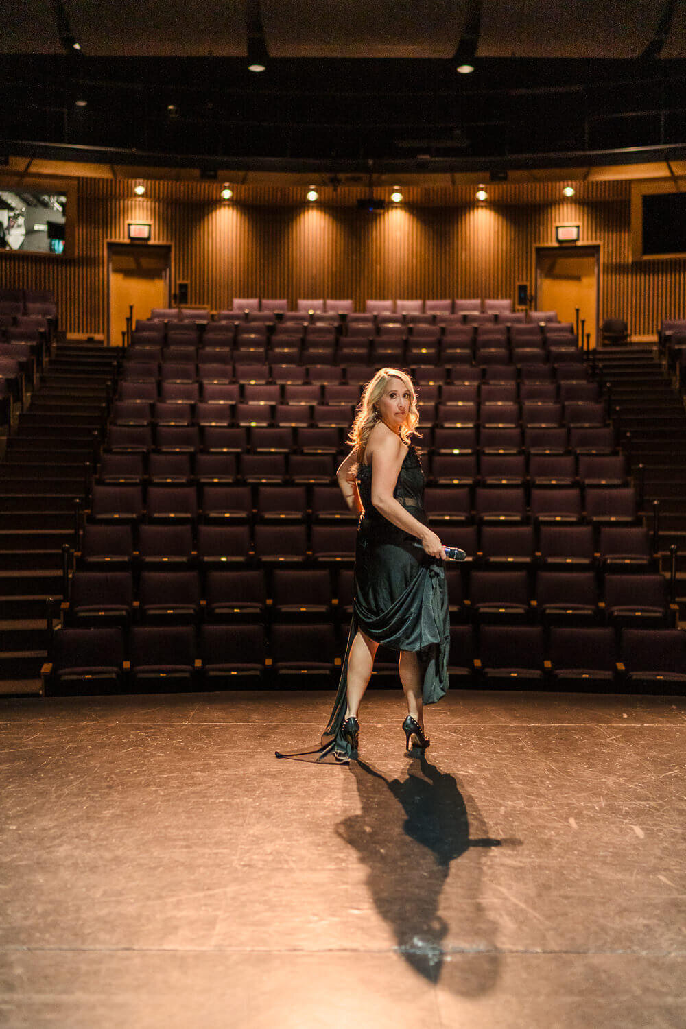 Woman in black dress on a theatre stage looking back over her shoulder at the camera