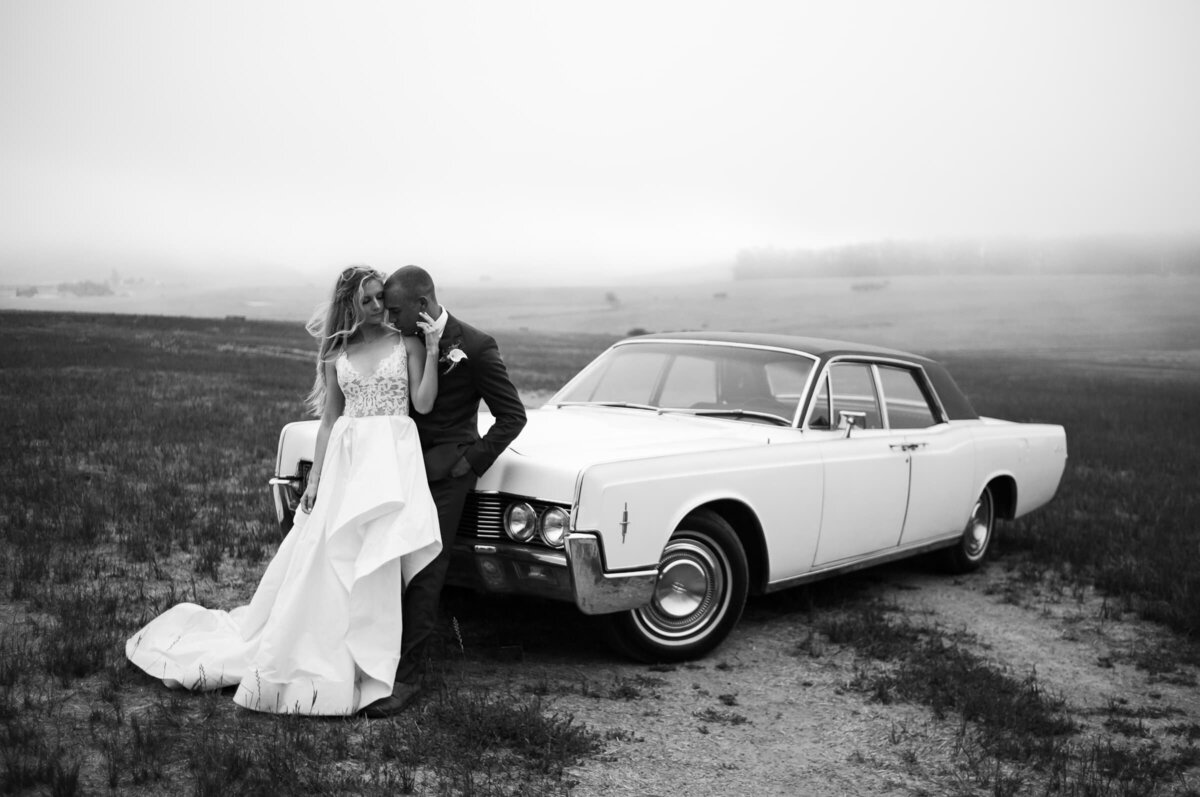 black and white portrait of newlyweds leaning on a white vintage car