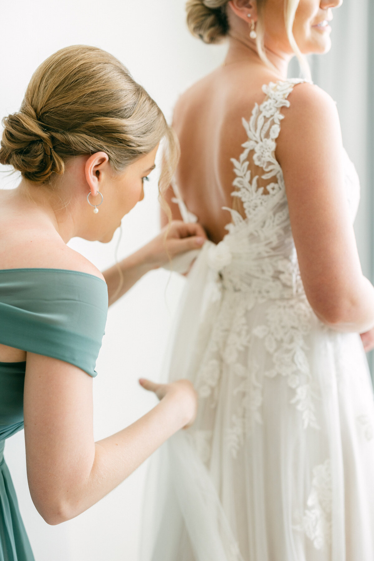Bridesmaid fastening bride’s lace gown during getting ready in Cancun, captured by Philadelphia wedding photographer.