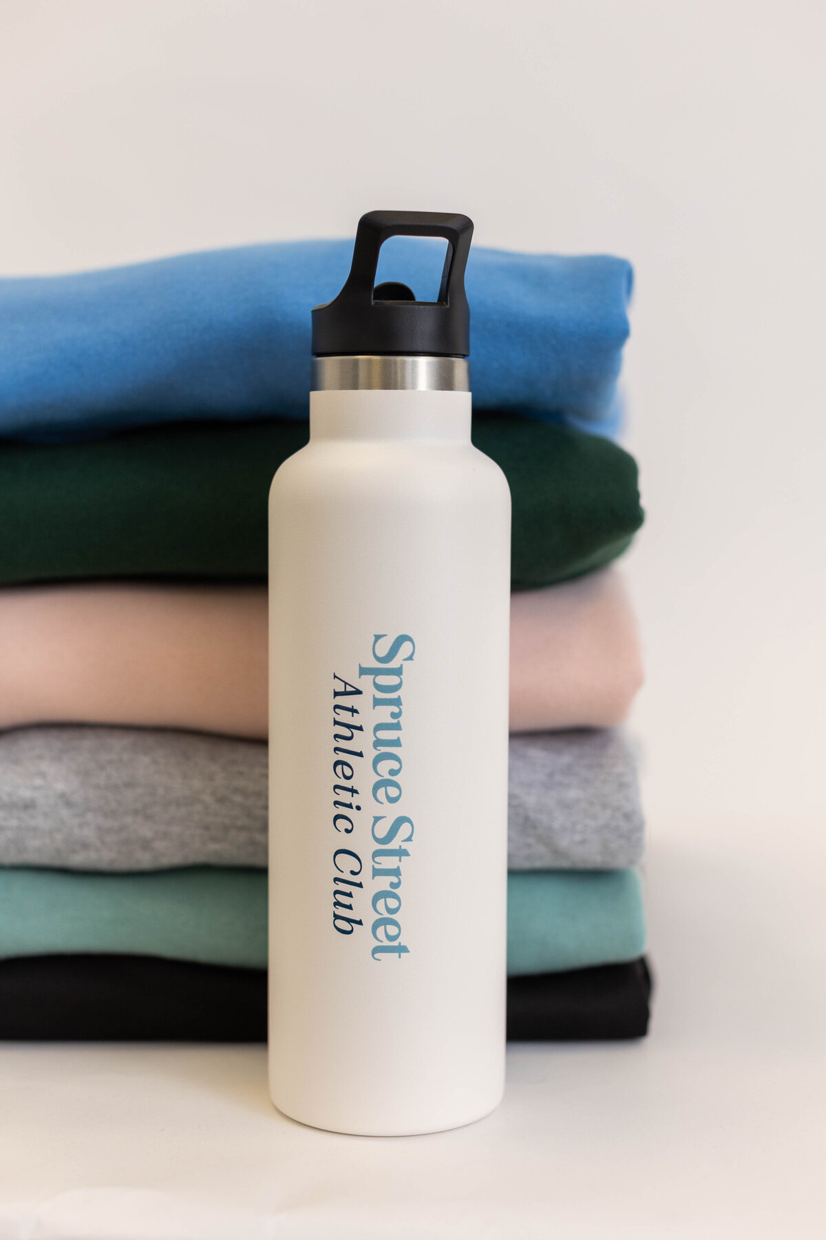 Branded water bottle in front of stacked folded seatshirts