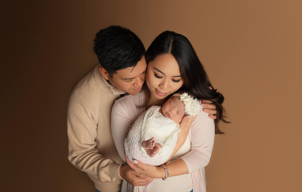 Couple holding and looking down at the infant girl at  Greater Toronto Newborn Photographer studio.