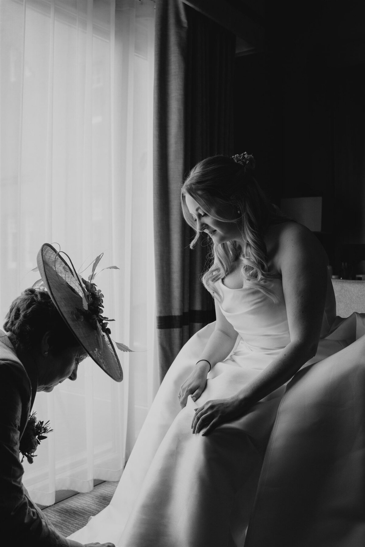A bride gets ready for her wedding as her mum kneels down to fit her shoes.