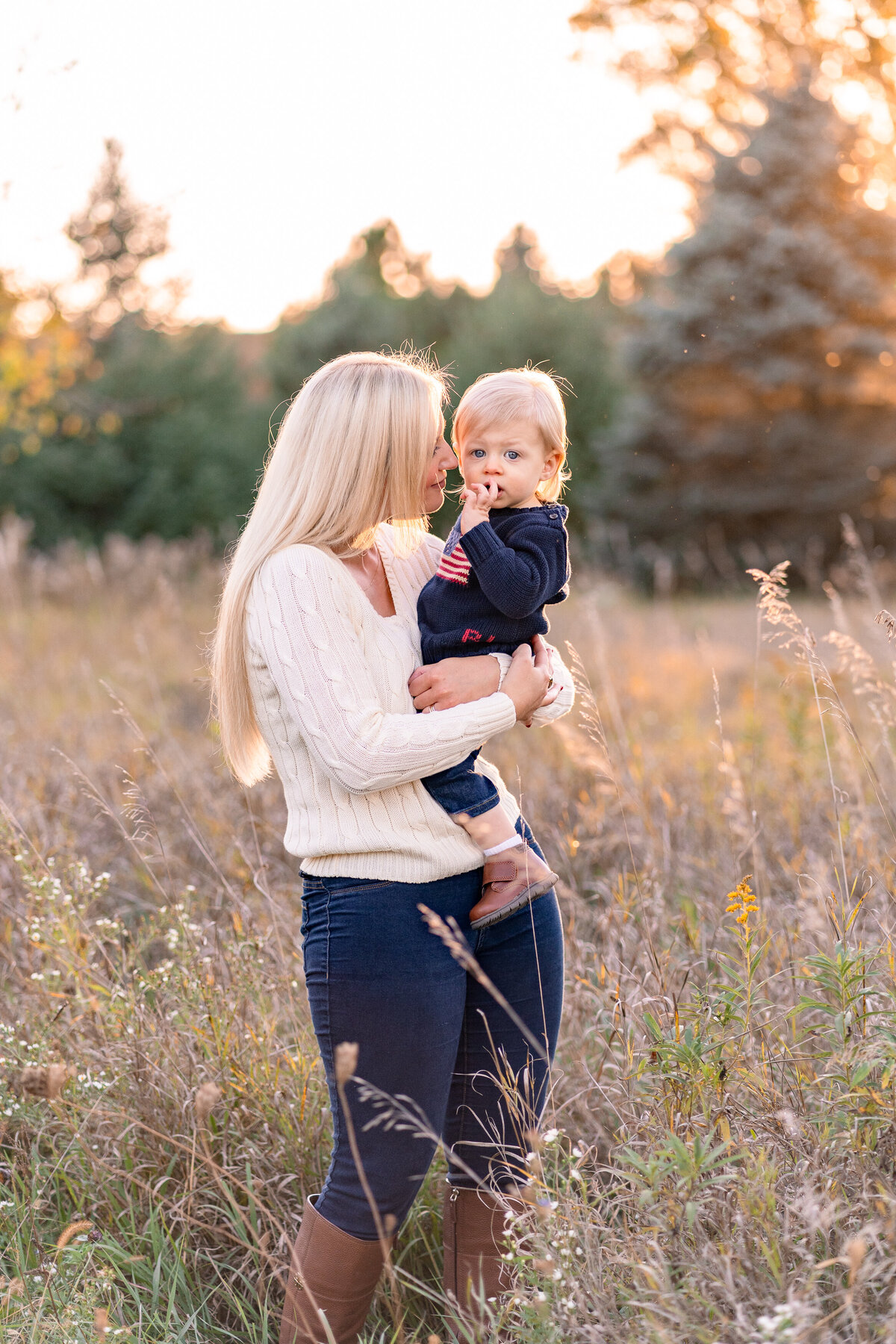 Mom placing nose to babys temple and smiling at baby in an open grassy field with wild flowers in Kensington Metropark milford Michigan