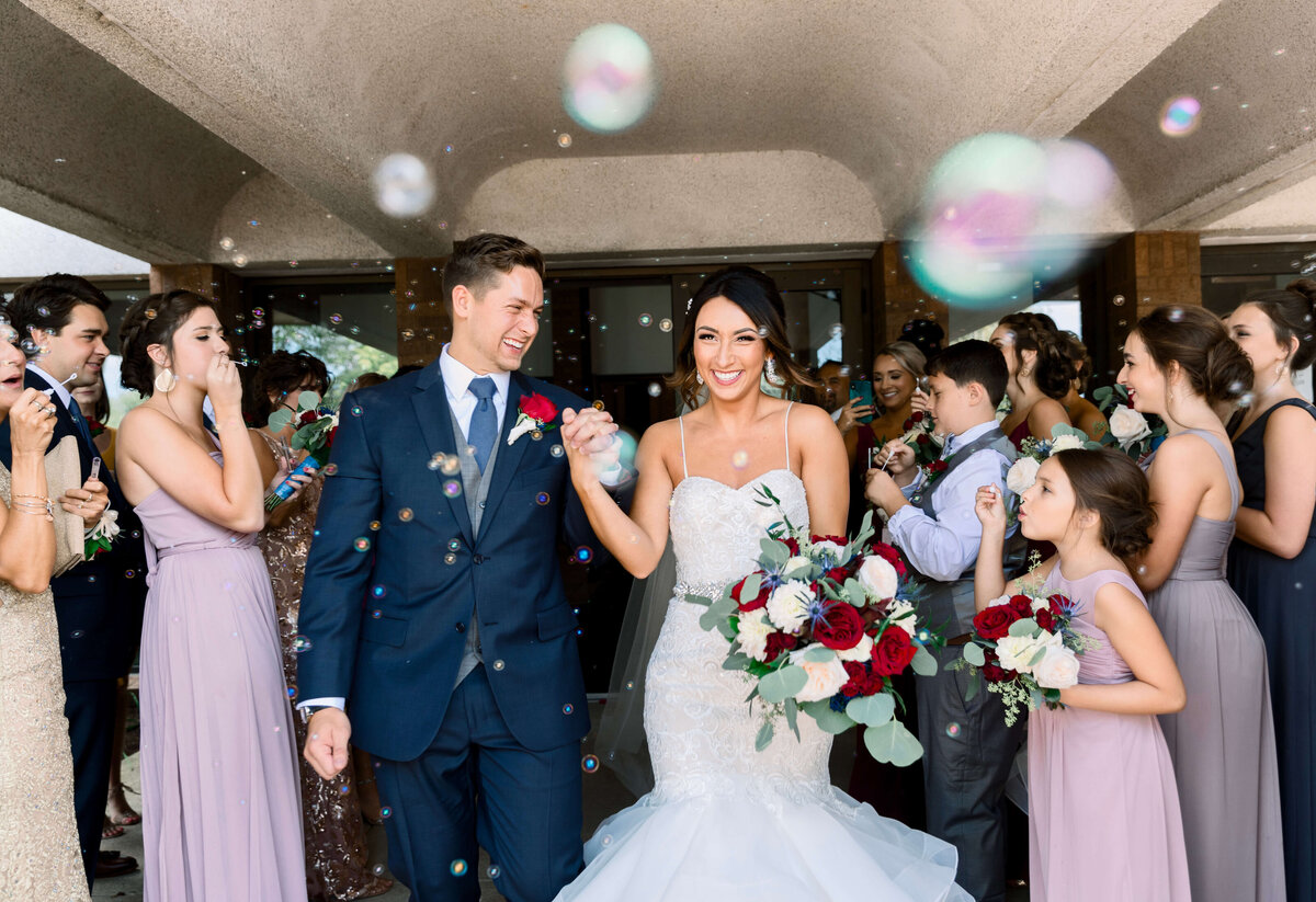 Photo of a bride and groom coming out of a church with guests blowing bubbles